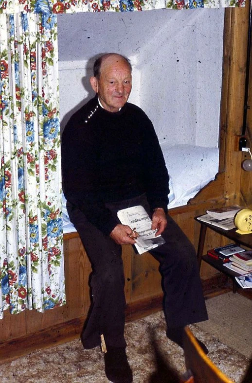 a man in black sweater sitting on bed holding a book