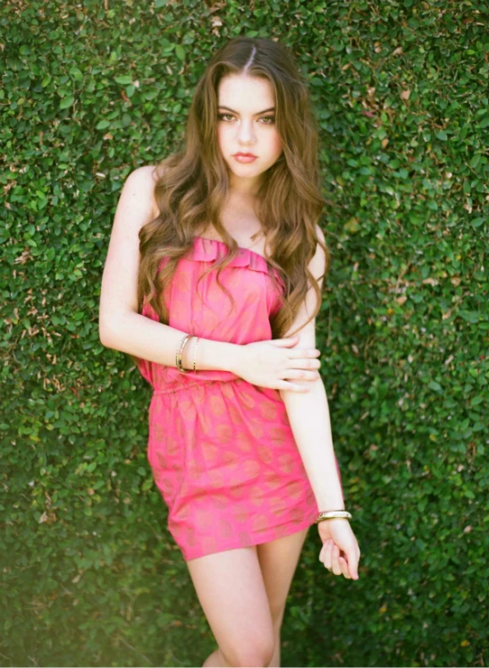 a pretty young lady leaning on some ivy