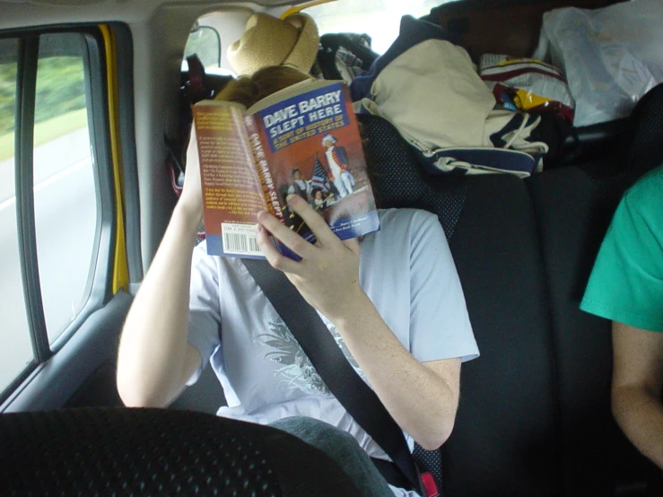 a woman that is in the back seat of a car reading a book