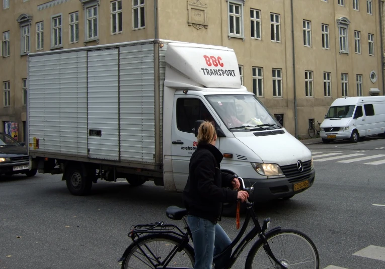 a lady is riding her bike behind a white truck