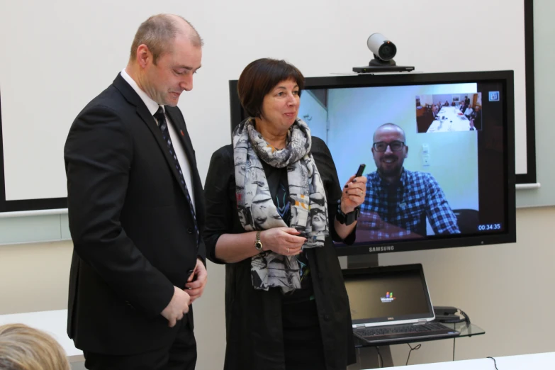 a man and woman watching a television with one holding a phone