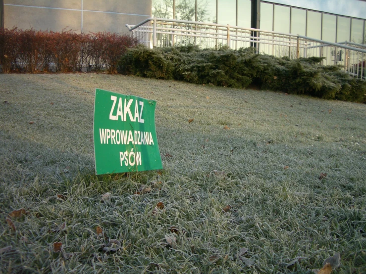 a green sign in the grass near some buildings