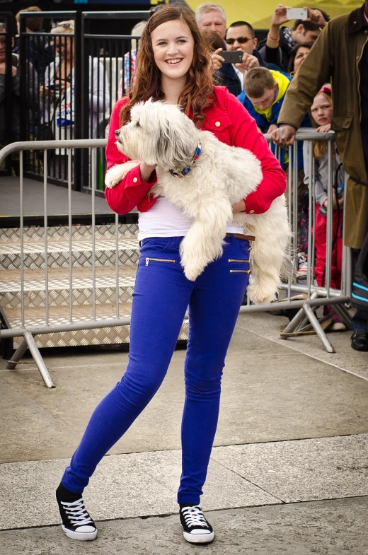 a young woman holds a small dog while standing on the sidewalk