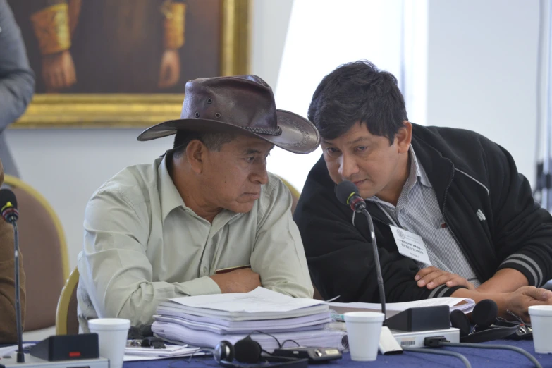 two men at a table with books, papers, and microphones