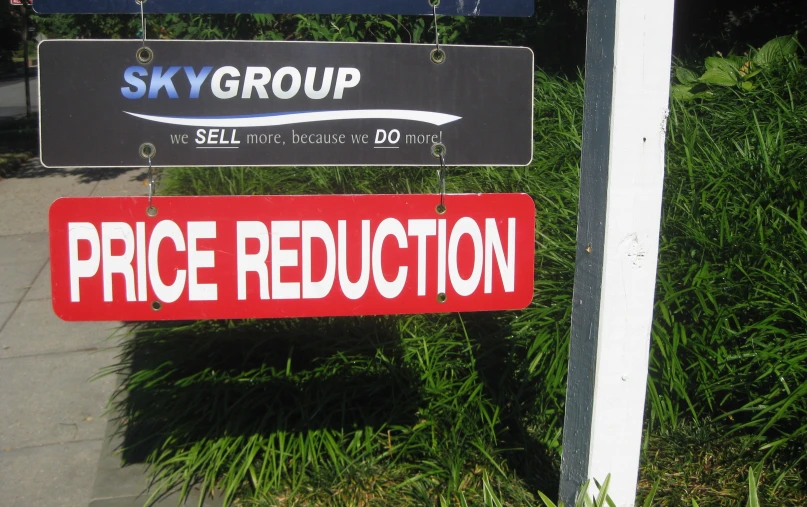 a red sign with black border on a street in front of bushes