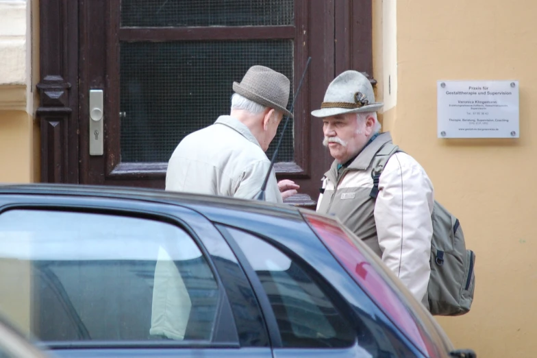two men in hats talking to each other next to a car