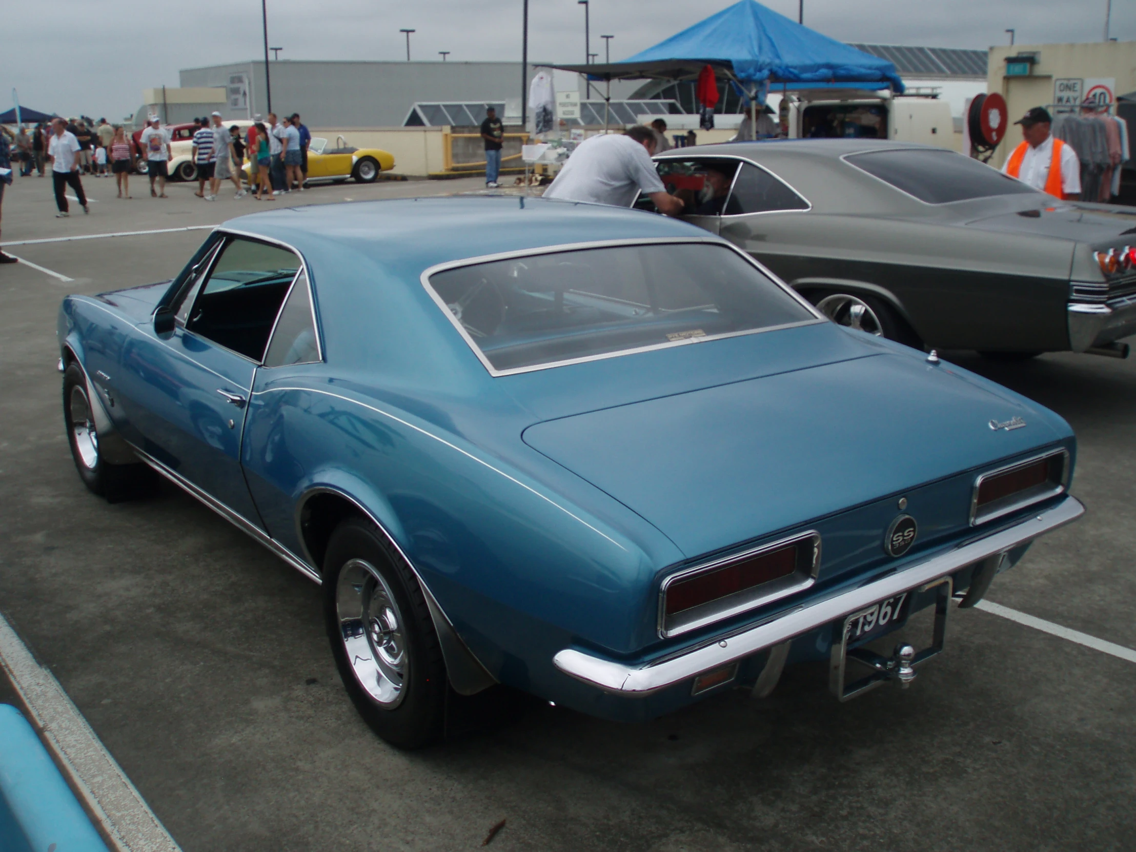 a vintage car is parked in the lot as people are around it