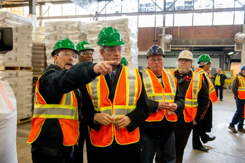 several men in hard hats and reflective vests are standing near pallets