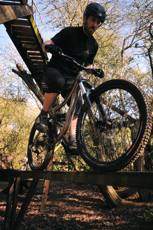 a man riding a bike over a wooden rail