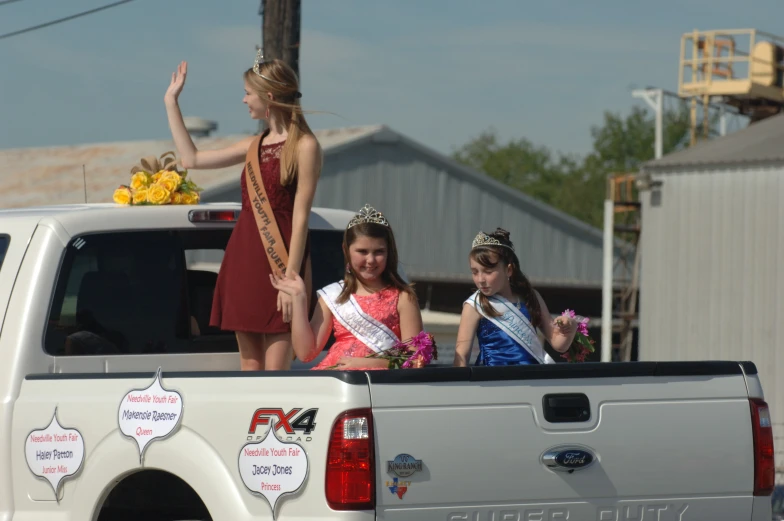 two girls in a white truck waving while two girls are waving out their hands