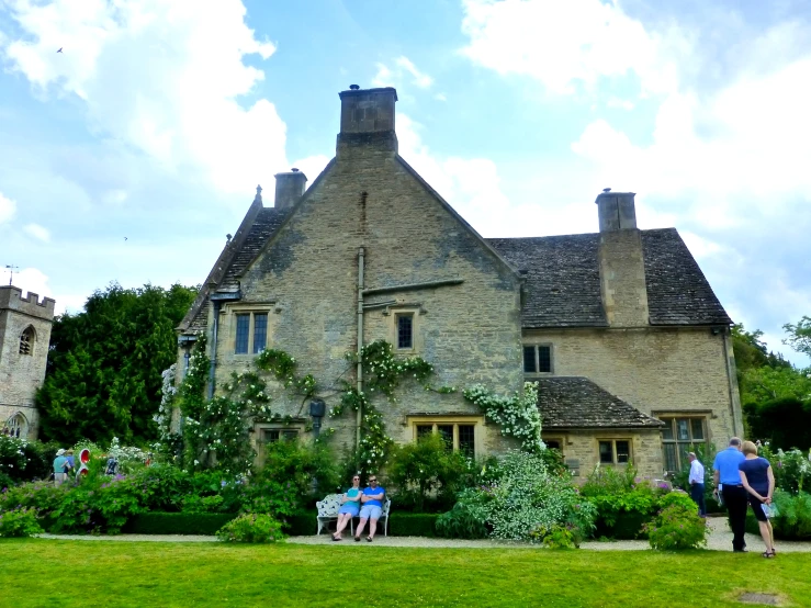 two people sitting on a bench in front of a stone house