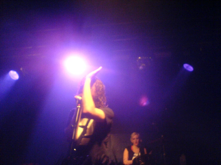 a woman in dark clothes standing on stage with her arms raised