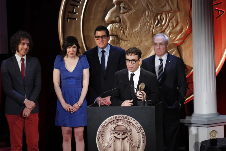 men and women are standing at a podium while one man gives a speech