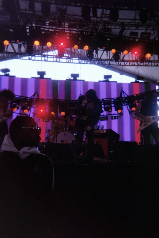 an audience with instruments in the foreground and a stage with large lights in the background