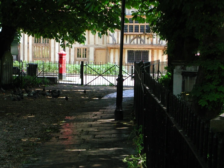 a view through a fence of an old fashioned building and a park with a bench in the foreground