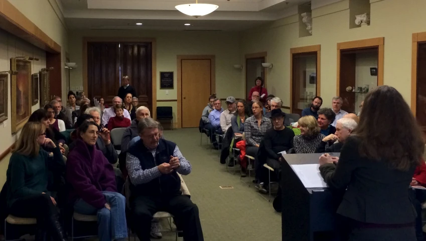 the room full of people are sitting in chairs, listening to speakers