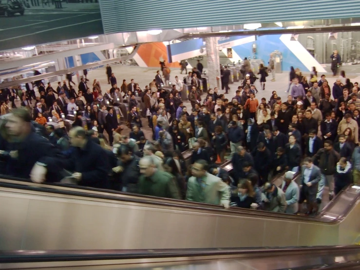 a large group of people moving down an escalator in a train station