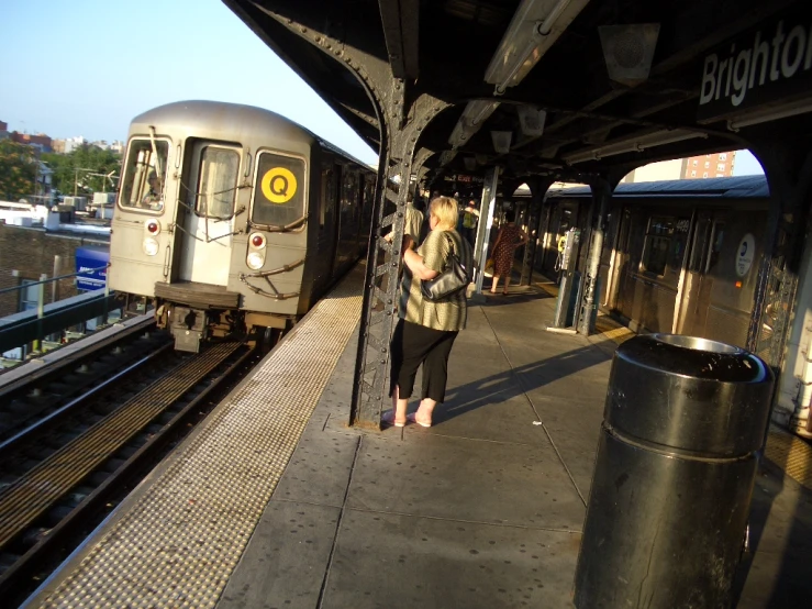 two people stand waiting on a platform as the train approaches