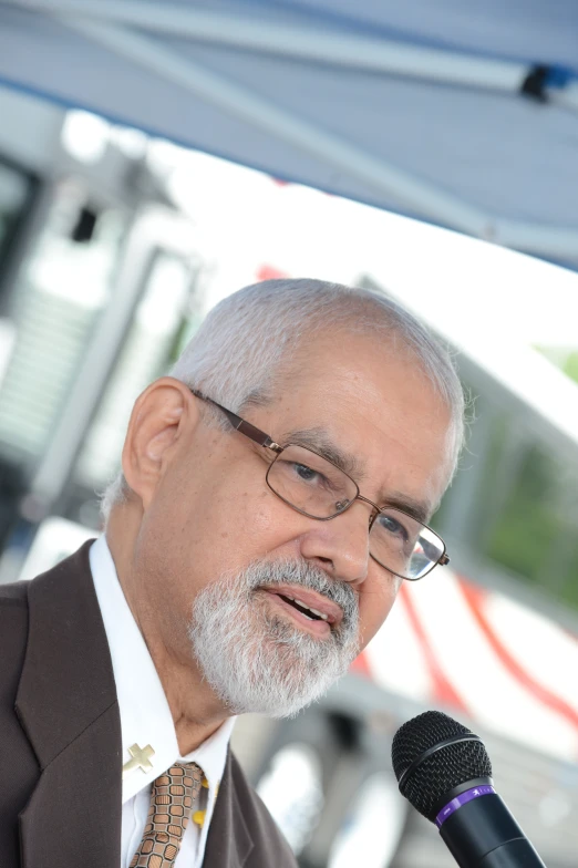 an older man in suit and glasses speaking into a microphone