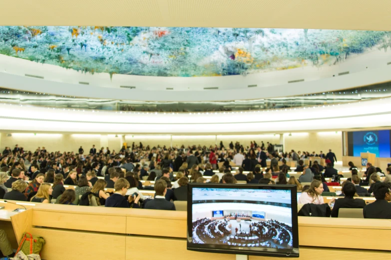 people are sitting in rows in a conference hall watching a television