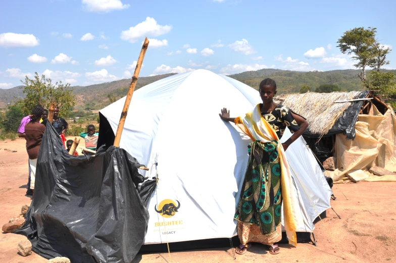 a woman stands outside of her tent with some people around her