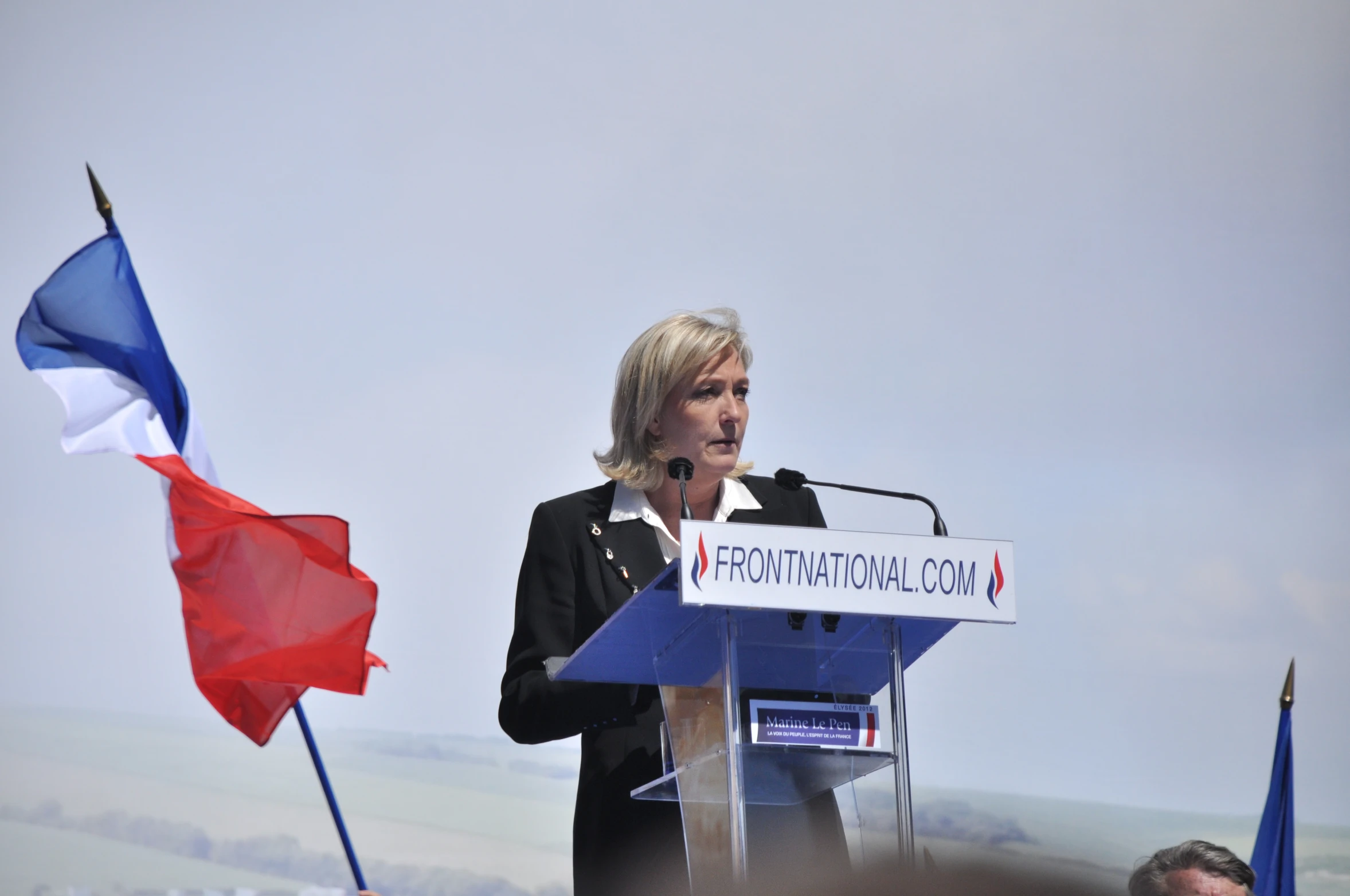 the woman speaking at a podium has a small flag in front of her