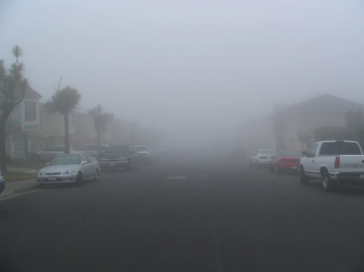 cars parked on a foggy street with cars behind them