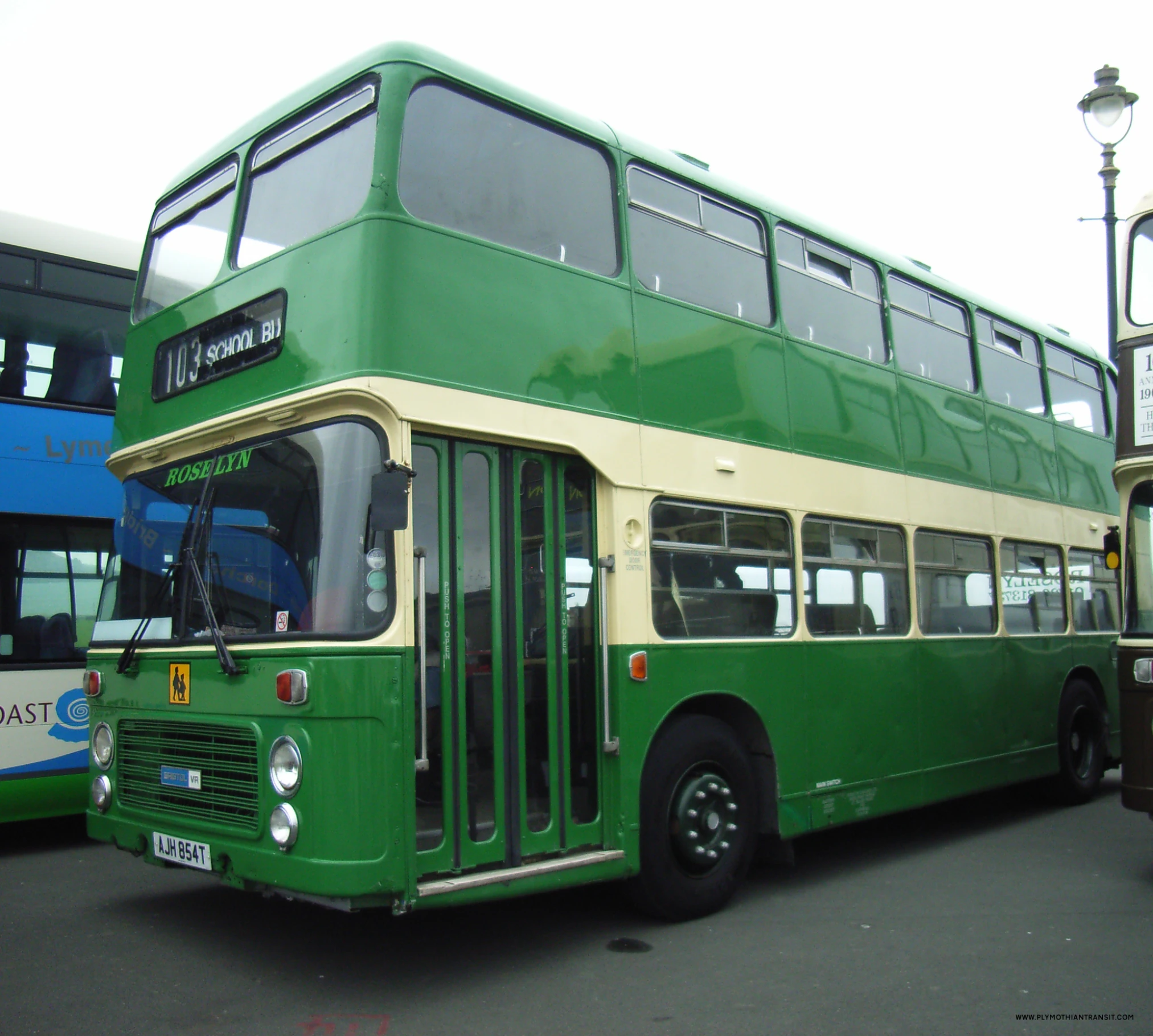 two buses are parked with one being green and the other is tan