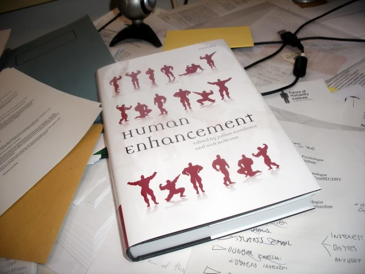 a book about human enharment sits atop piles of papers