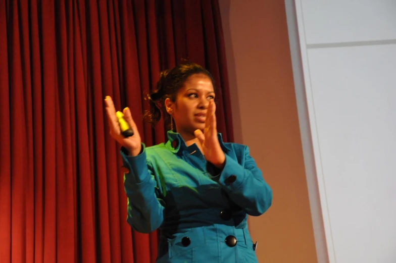 a woman standing up in front of red curtains holding a finger to her lips