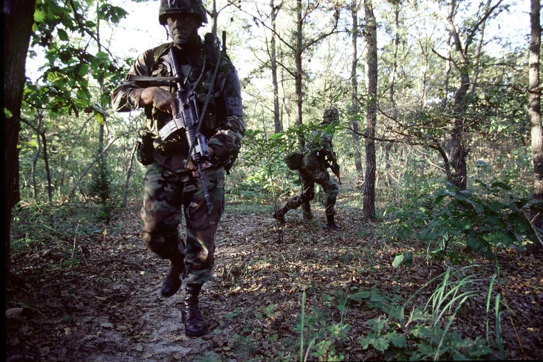 men in camouflage with gun running through forest