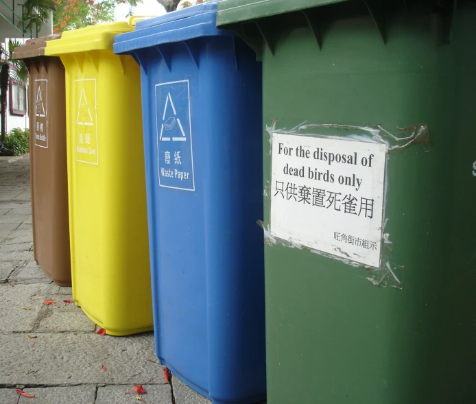 a row of trash cans in different colors on the sidewalk
