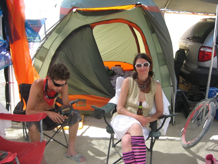 two men sitting in chairs next to a tent