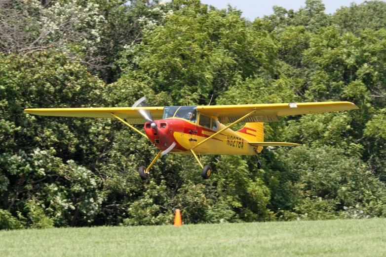 a small yellow and red plane on runway in grassy area next to trees