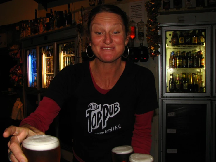 an older lady holding beer glasses in front of a display of bottles and glasses