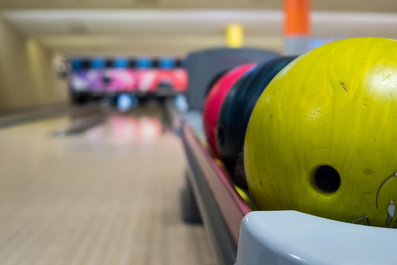 a yellow ball with a black one and its wheels leaning on a bowling alley