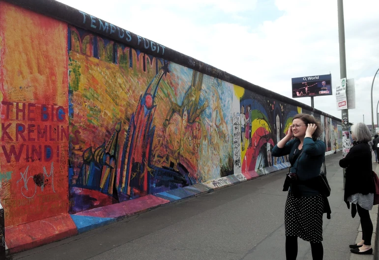 several women on a cellphone stand near a graffiti wall