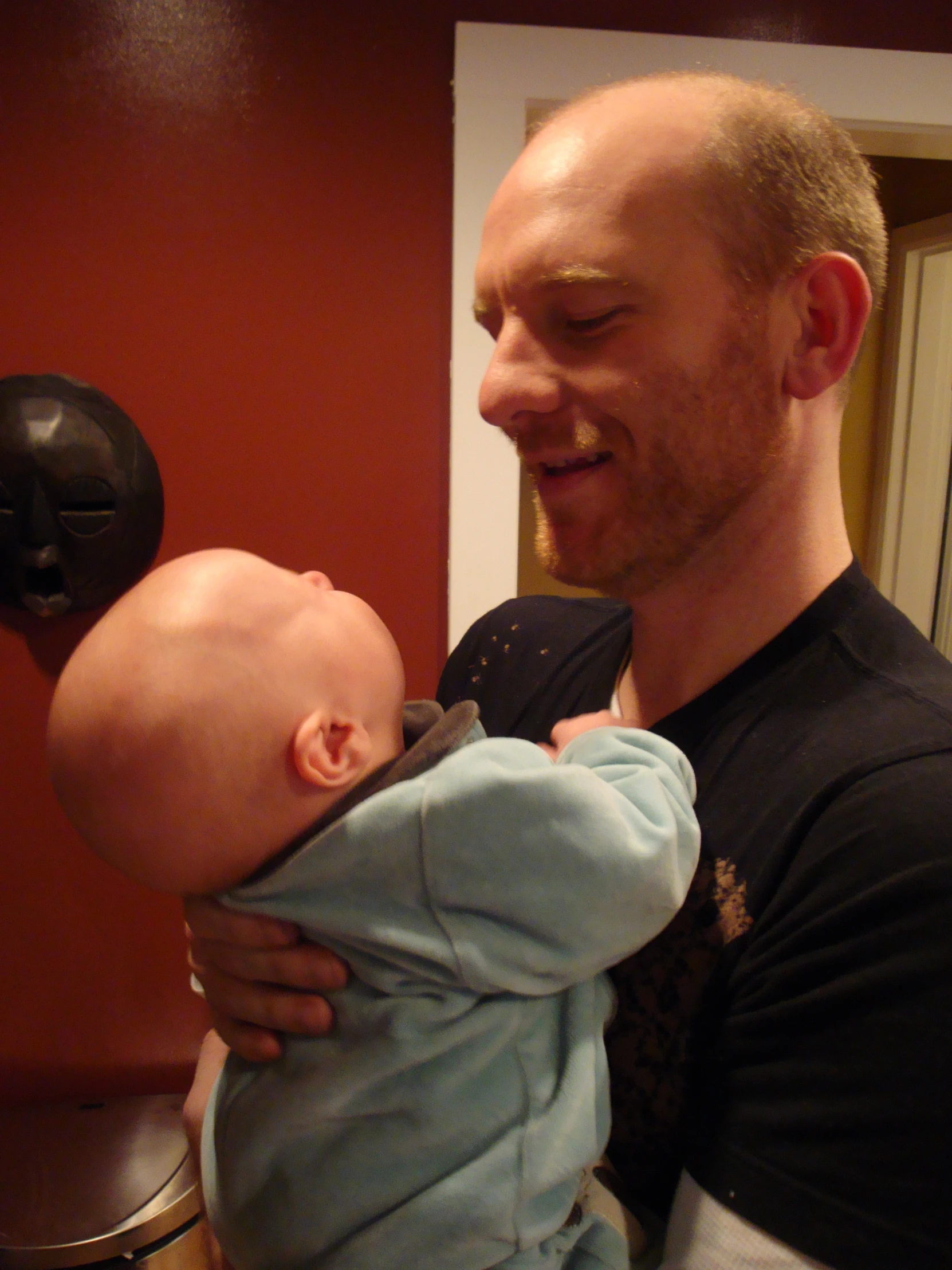 a man holding up a baby next to a red wall