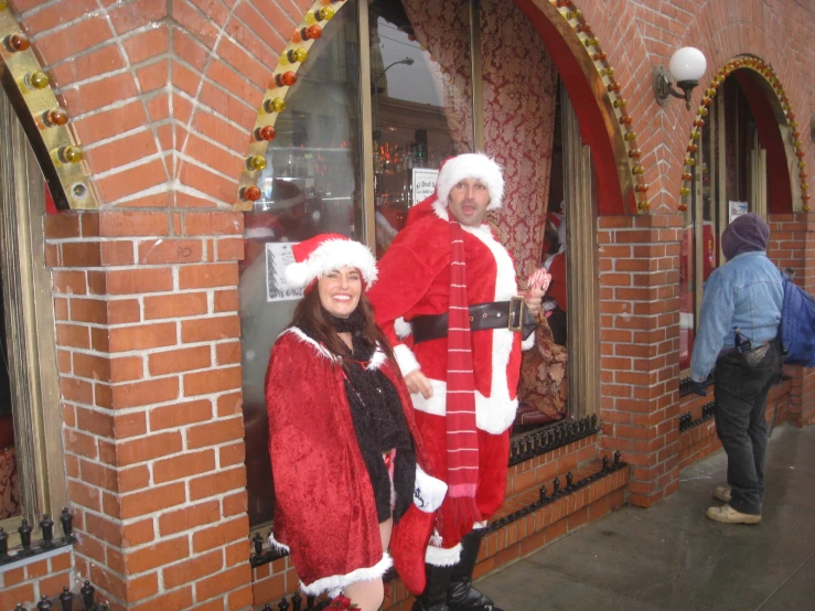 a couple poses next to a red brick building dressed up for the holidays