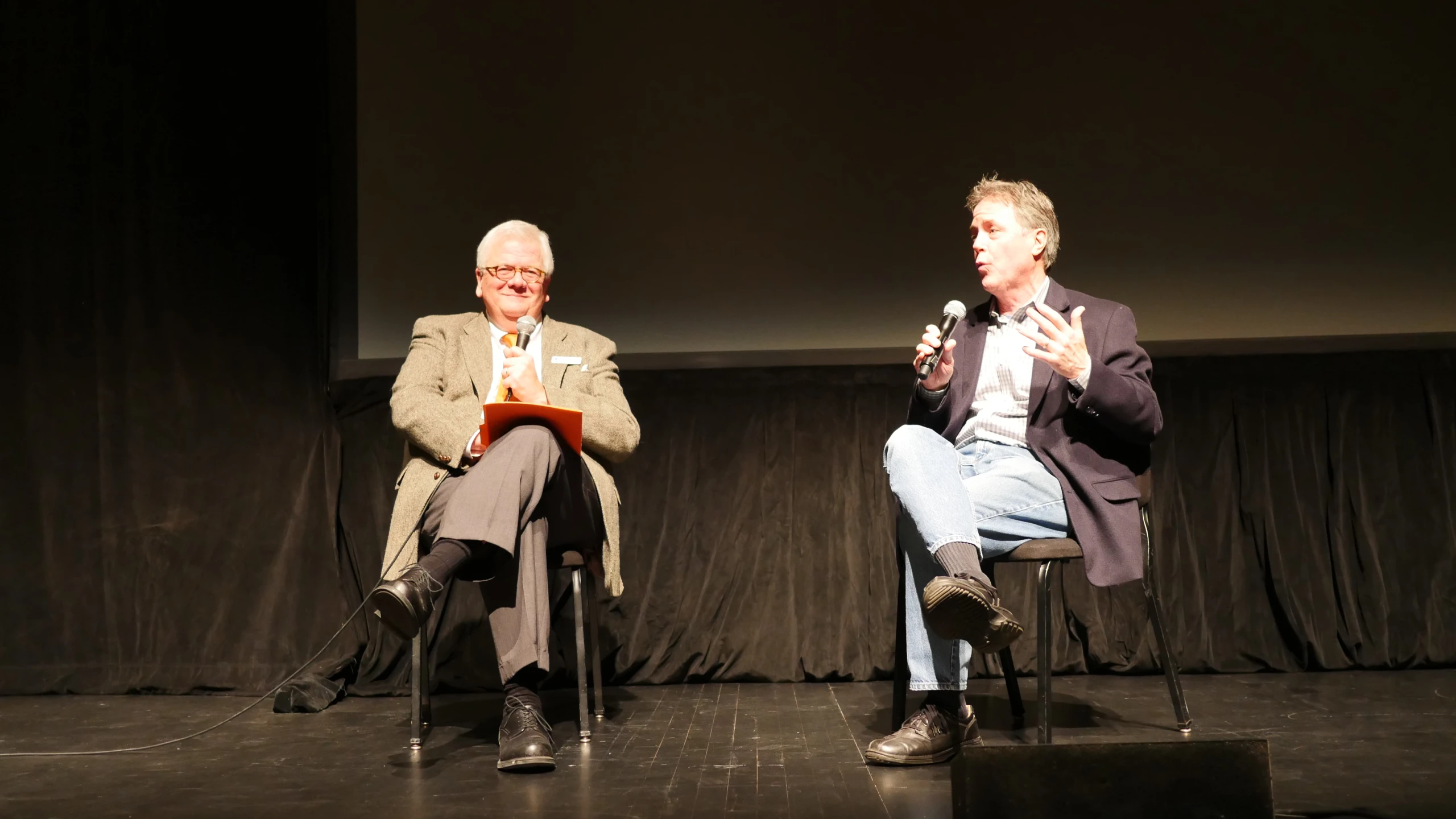 two men sitting on chairs while one is holding soing