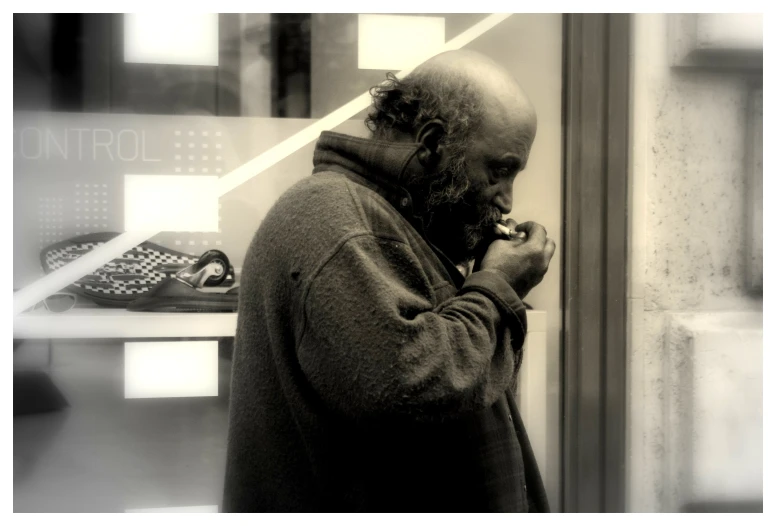 man with beard and sweater texting on phone while standing outside store