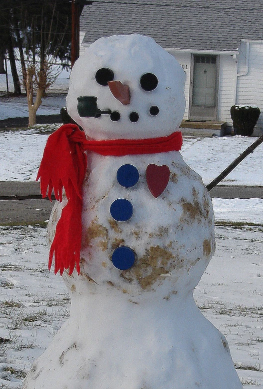 a snowman wearing a red scarf and hat is next to a house