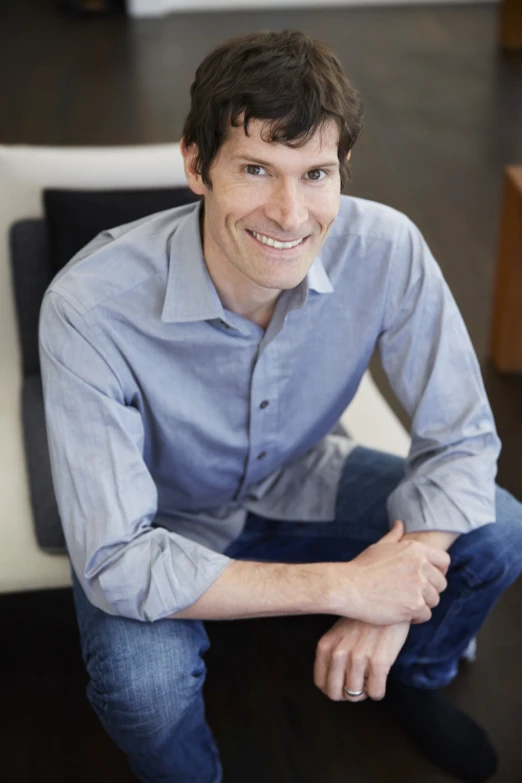 a man wearing a blue shirt sitting on a chair smiling