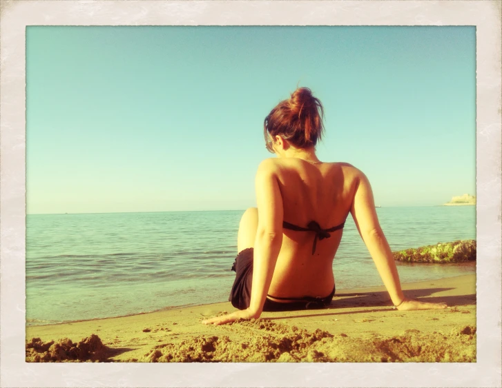 a woman in a bikini sitting at the ocean