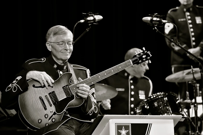 man with glasses playing guitar and band at the podium