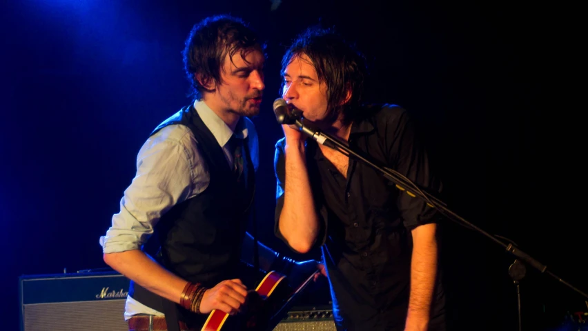 two men singing into microphones while holding guitars