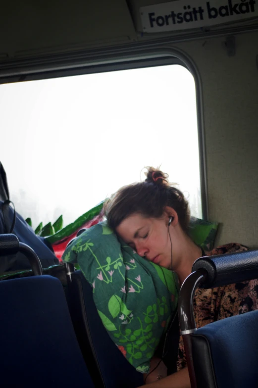 a woman sleeping on a bus seat, while listening to ear buds