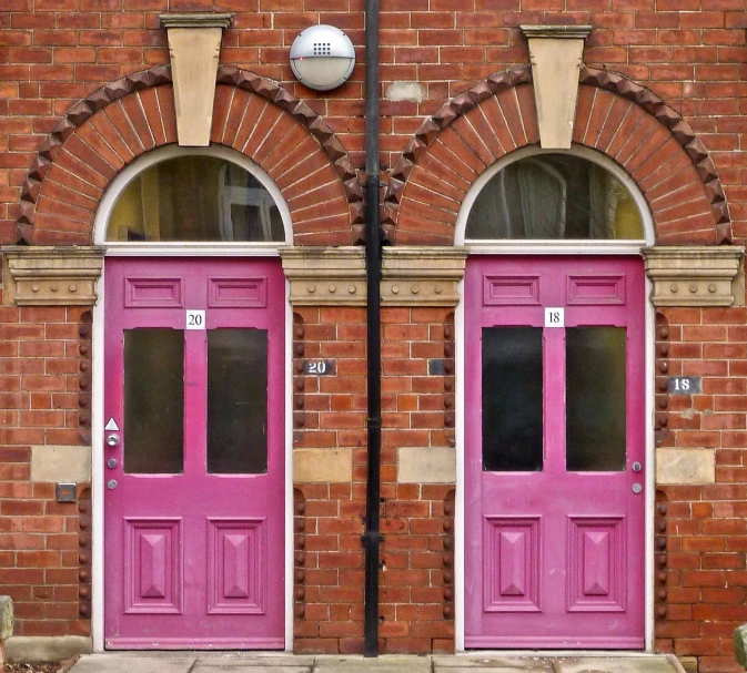 two very pretty pink doors by some brick buildings