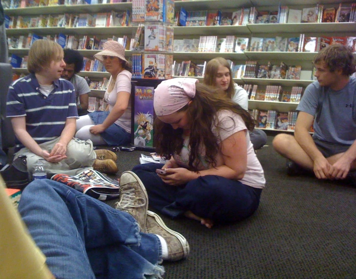 group of teens sitting on the ground and looking at their cellphones in a liry