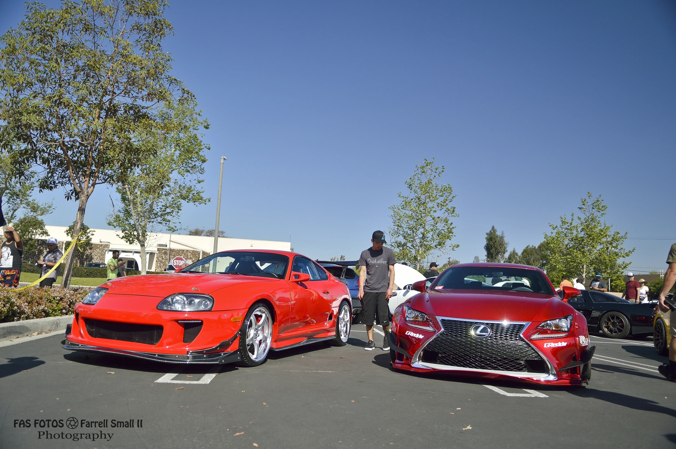 two cars in a parking lot with people standing around them